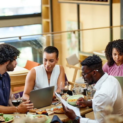 A group of casual businesspeople is sitting in a restaurant for a meeting, discussing a project while having dinner.